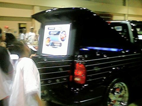 1998 Ford Taurus - A black pickup truck is displayed with a screen on its tailgate at an indoor event.