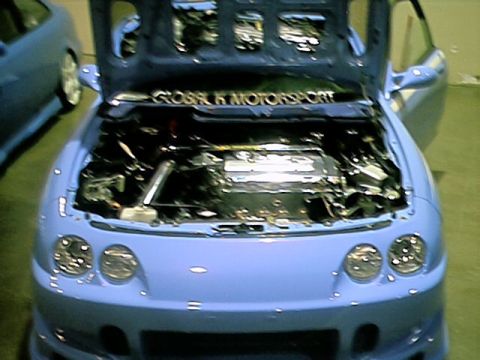 1998 Ford Taurus - Engine bay of a light blue car, with another vehicle in the background. Text on hood reads GLOBAL K MOTORSPORT.