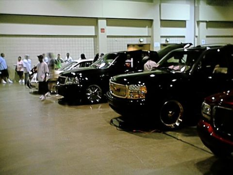 1998 Ford Taurus - A collection of customized vehicles are on display inside a building, with attendees walking around.