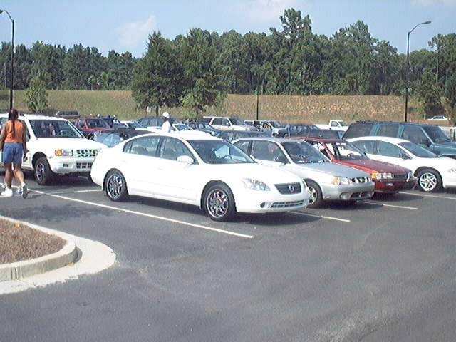 Parking lot scene with a person walking past several cars parked in rows