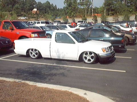 1998 Ford Taurus - A lowered white pickup truck with distinctive custom wheels is parked in a lot full of other vehicles.