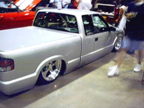 1998 Ford Taurus - A silver pickup truck with custom wheels and a lowered stance is displayed at a car show.