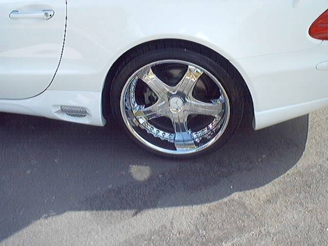White car side view showing a chrome five-spoke wheel and part of the door