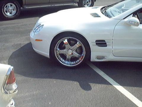 1998 Ford Taurus - A white convertible sports car is parked next to another vehicle, showing off its custom chrome wheels and distinctive side vents.
