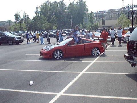 1998 Ford Taurus - A red convertible sports car is parked in a lot with several people gathered around.