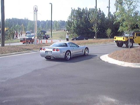 1998 Ford Taurus - A silver Chevrolet Corvette C5 is seen from the rear, navigating a curve on a road with other vehicles present.
