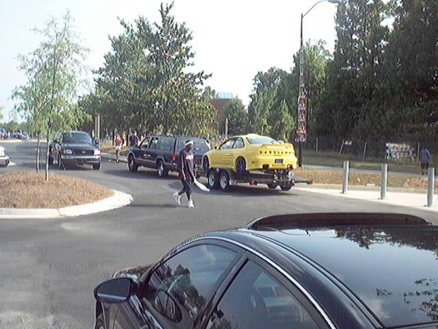 Yellow custom coupe on an open trailer being towed behind a dark SUV