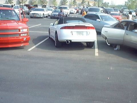 1998 Ford Taurus - A white convertible sports car is parked in a lot with other vehicles.