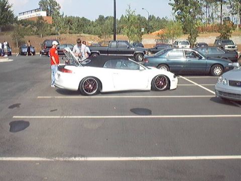 1998 Ford Taurus - A white convertible sports car with custom wheels is parked in a lot, with other vehicles visible in the background.