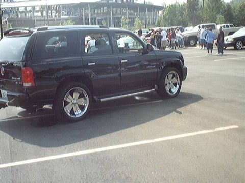 1998 Ford Taurus - A black Cadillac Escalade is parked in a lot with other vehicles and people visible in the background.
