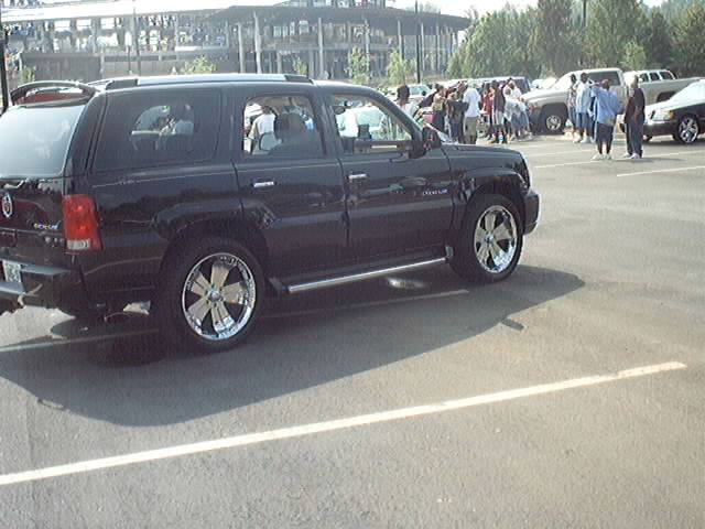 black Cadillac Escalade parked in lot, other cars and people in background