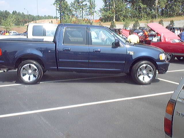 Blue four-door pickup truck with chrome wheels parked in a lot