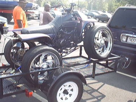 1998 Ford Taurus - A custom ATV with oversized chrome wheels is loaded onto a trailer, parked next to a dark-colored SUV.