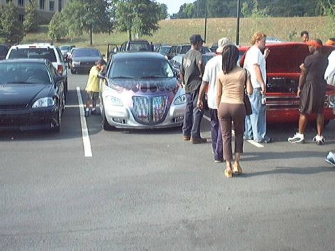 1998 Ford Taurus - Several people stand around a customized sedan in a parking lot, with other vehicles visible in the background.
