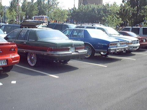 1998 Ford Taurus - Several cars are parked in a lot, including a green sedan with custom wheels.