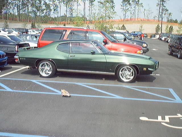 Dark green Pontiac GTO coupe, driver-side view on polished five-spoke wheels in a parking lot