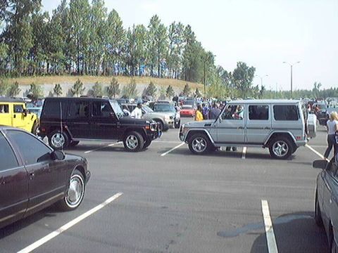 1998 Ford Taurus - A silver Mercedes-Benz G-Wagen is seen parked in a lot alongside other vehicles and trees in the background.