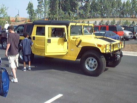 1998 Ford Taurus - A yellow Hummer H1 is parked on asphalt with its driver's door open, and other vehicles are visible in the background.