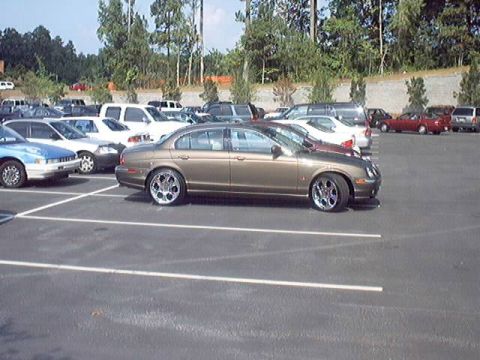 1998 Ford Taurus - A gold sedan with custom rims is parked in a lot full of other vehicles.