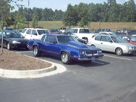 1998 Ford Taurus - A blue coupe with a prominent hood scoop is seen in a parking lot with other vehicles.