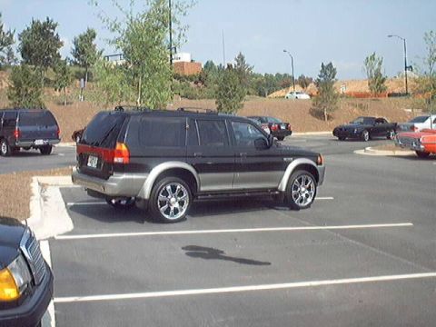 1998 Ford Taurus - A black Mitsubishi Montero Sport SUV is parked in a lot with other cars around it.