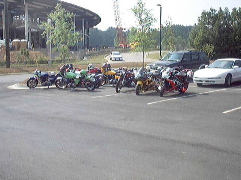 1998 Ford Taurus - A variety of motorcycles and a white car are parked in a lot near a building.