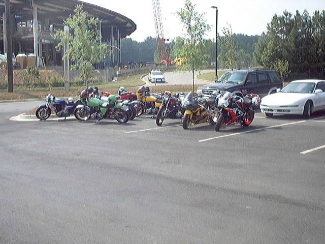 Several motorcycles and a white car parked in a lot