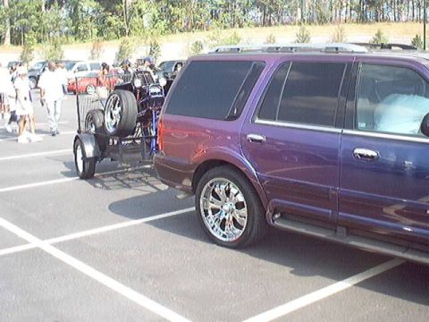 1998 Ford Taurus - SUV towing a trailer with spare tires at a car show.