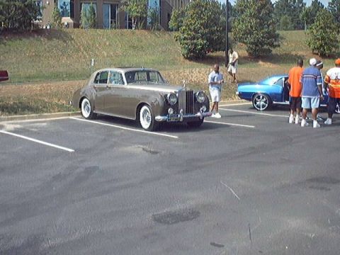 1998 Ford Taurus - A classic Rolls-Royce Silver Cloud is parked next to a blue muscle car at an outdoor event.