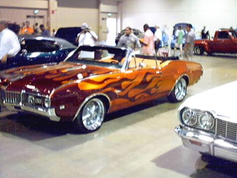 1998 Ford Taurus - A custom orange convertible with flame graphics is displayed at a car show.