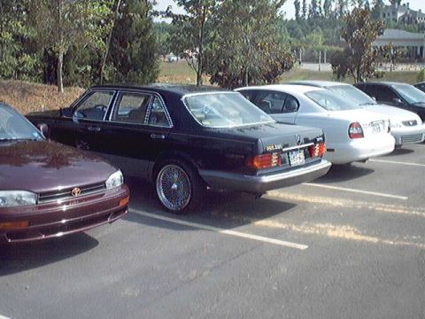 1998 Ford Taurus - A dark sedan with distinctive wire wheels is parked in a lot alongside other vehicles.