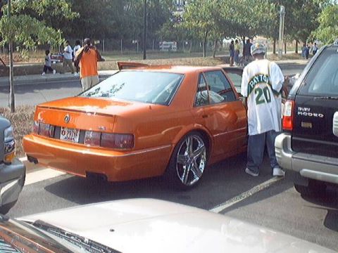 1998 Ford Taurus - Orange sedan with custom wheels and a black SUV at a car show.