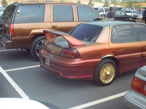 1998 Ford Taurus - An orange sedan with a spoiler and gold wire wheels is parked next to a brown SUV.
