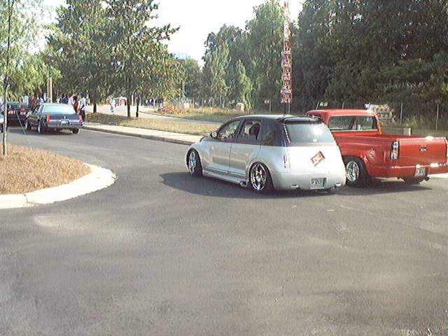 Silver PT Cruiser with custom wheels and a red pickup truck parked next to it on a street