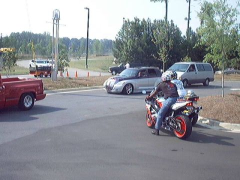 1998 Ford Taurus - A motorcycle with two riders passes by other vehicles on a sunny day.