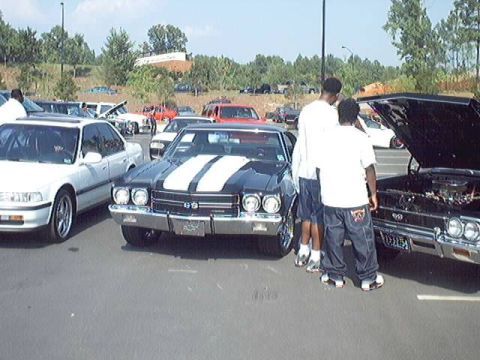 1998 Ford Taurus - Several cars are parked in an outdoor lot, including a classic black muscle car with racing stripes.