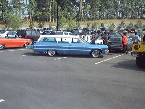 1998 Ford Taurus - Several cars are parked in a lot, including a blue station wagon and an orange convertible.