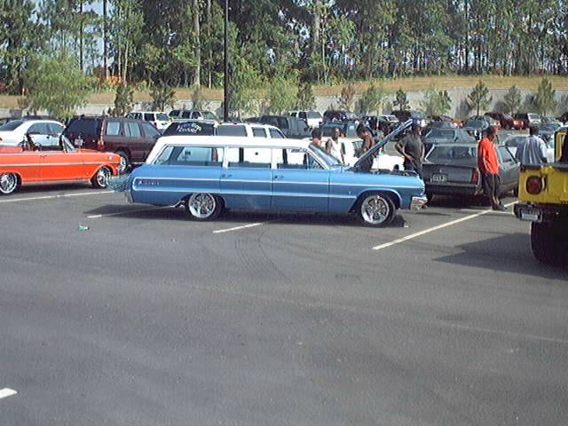 Lowered blue and white 1960s Chevrolet Impala wagon with hood up at a car show lot