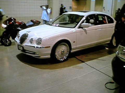 1998 Ford Taurus - A white Jaguar S-Type sedan is parked indoors next to a motorcycle, with people in the background.