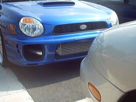 1998 Ford Taurus - A blue Subaru Impreza WRX is parked next to a silver car, showing its front bumper and intercooler.