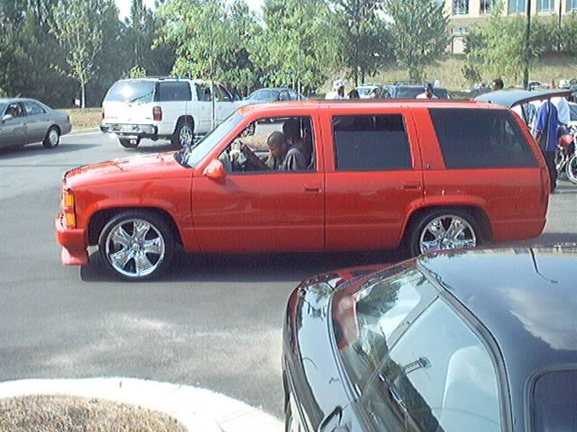 red SUV driving on road, white truck and silver car in background