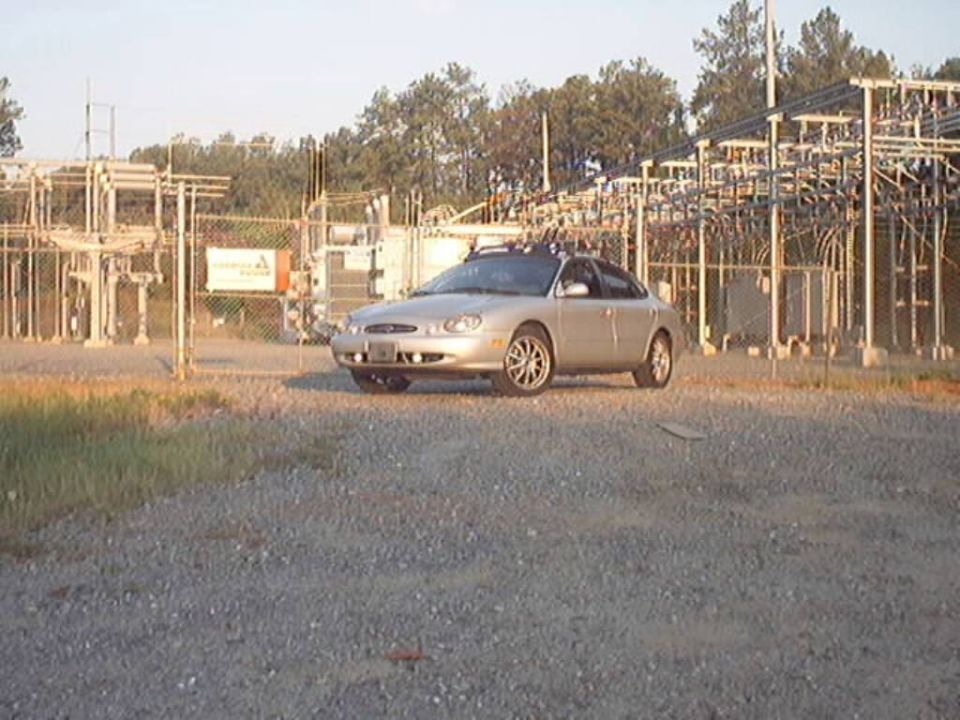 Gold Ford Taurus sedan on gravel lot in front of electrical substation