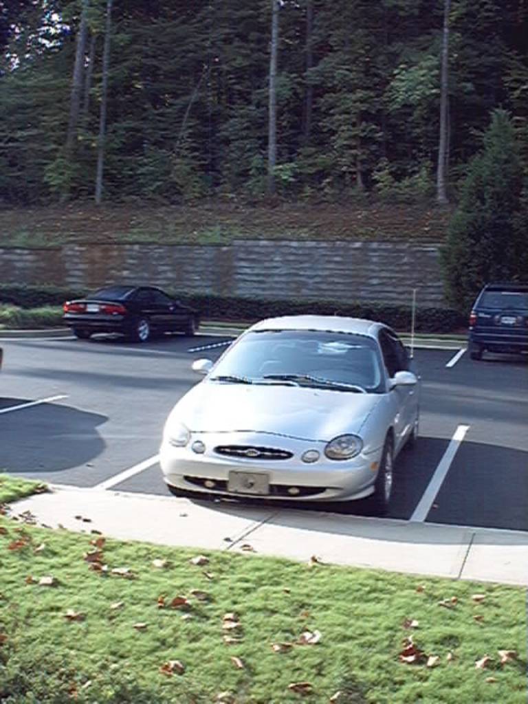 Silver Ford Taurus sedan parked nose-in in a lot, viewed from above at a front angle
