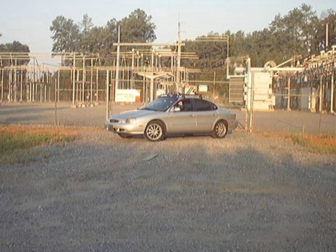 1998 Ford Taurus - Side view of a silver/champagne Ford Taurus sedan parked on gravel in front of an electrical substation, fitted with multi-spoke alloy whee…