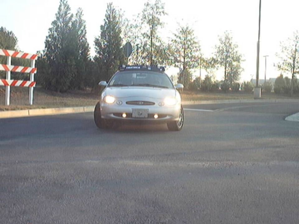Silver Ford Taurus front view, headlights on, roof light bar, on pavement
