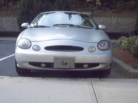 1998 Ford Taurus - Head-on front view of a silver oval-styled Ford Taurus sedan parked at a curb, showing its oval grille opening, rounded composite headlight…