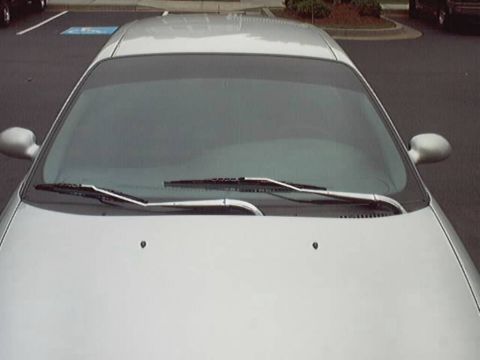 1998 Ford Taurus - Close overhead front view of a silver sedan's hood, cowl and windshield in a parking lot, showing chrome-finished windshield wiper arms and…
