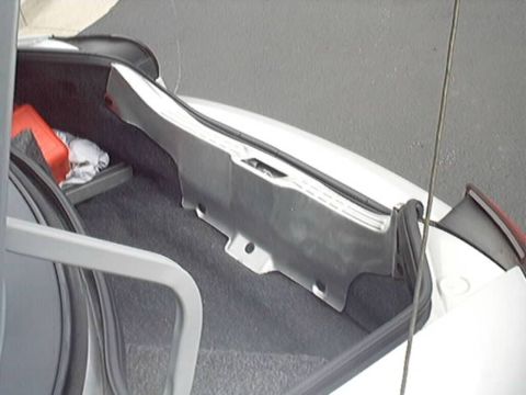 1998 Ford Taurus - Close-up of an open vehicle trunk showing a large gray molded plastic interior trim panel resting on gray carpet, with a red object and whi…