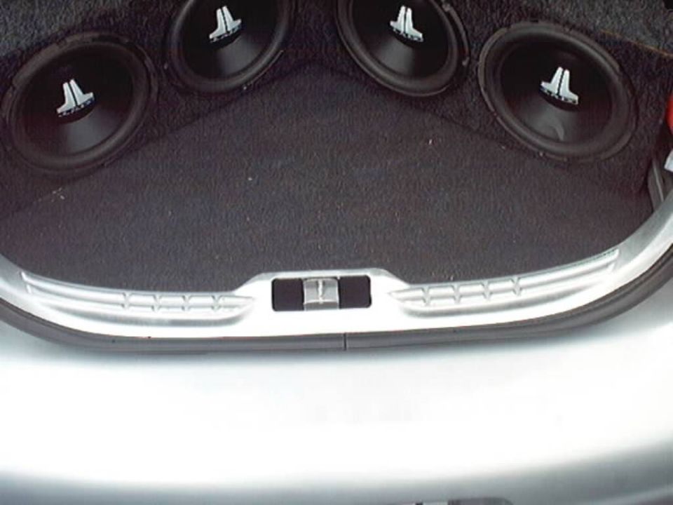 Four JL Audio subwoofers in a carpeted custom trunk enclosure of a silver sedan
