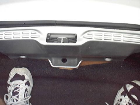 1998 Ford Taurus - Looking down at the stamped underside of a silver trunk lid and its center latch mechanism above black trunk carpet, with the photographer'…